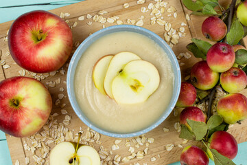 Oatmeal porridge for the baby from ground cereals in a blue bowl, red ripe apples on a wooden board. Baby's first complementary food, baby nutrition.