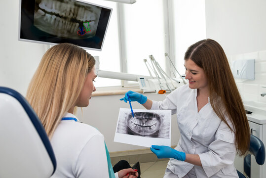 The dentist shows the x-ray image to the patient. People, medicine, dentistry, technology and healthcare concept.