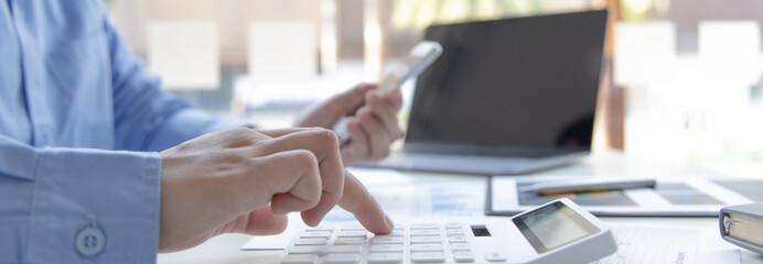 Asian male employees are analyzing market data via smartphones and have laptops to calculate the...
