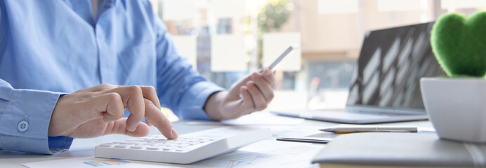 Asian male employees are analyzing market data via smartphones and have laptops to calculate the company's finances In a private office at home, Working at home and new normal concept.