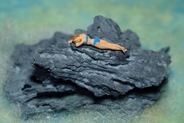 Miniature people toy figure photography. Teenage girl relaxing, lying on the coral. Summer holiday concept