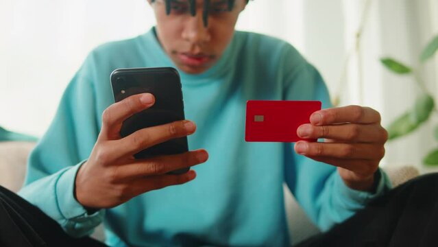 African American man using credit card and smartphone, shopping in app. Young guy buying clothes in application, online order, food delivery.