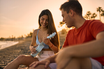 young woman sitting on the sand friend and playing her ukelele at the beach while sunset on a summer day