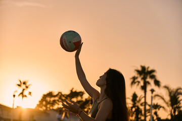 young spanish brunette woman playing volleyball at the beach while sunset