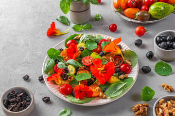 Summer salad with nasturtium flowers, tomatoes, olives, raisins and nuts on gray background. Healthy diet food