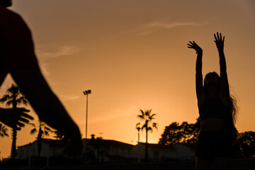 young spanish brunette woman playing volleyball with her boyfriend at the beach while sunset
