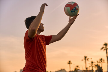 young man playing volleyball at the beach on a summer-day sunset