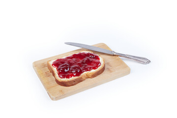 a piece of white bread with strawberry jam and a silver knife, isolated on white background