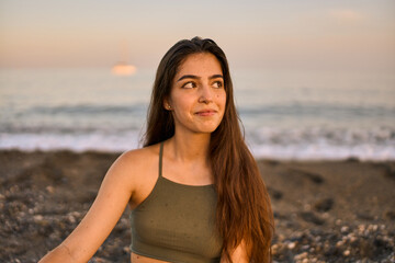 portrait of a young spanish tanned woman wearing a green top sitting in front of the sea at the beach on a summer day