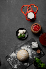 Products for cooking pizza and salad on a dark background. Fresh vegetables, sauces and herbs with spices.