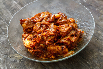Pieces of chicken in sauce fried in a glass plate on a dark wooden table.
