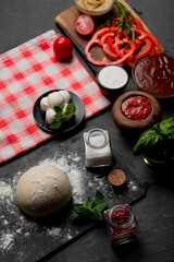 Products for cooking pizza and salad on a dark background. Fresh vegetables, sauces and herbs with spices.