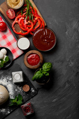 Products for cooking pizza and salad on a dark background. Fresh vegetables, sauces and herbs with spices.
