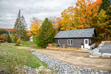 Exterior of a small lakeside holiday cabin with colourful trees in background on a cloudy autumn day