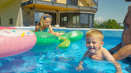 CLOSE UP: Smiling little boy floating in backyard swimming pool learning to swim