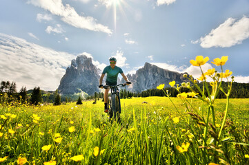 Fototapeta na wymiar Mountain biking through a sea of ​​yellow flowers with mountains in the background