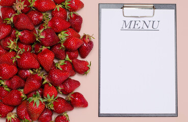 Juicy, ripe strawberries are laid out on a pink background with a tablet for recording the menu. Copy Space.