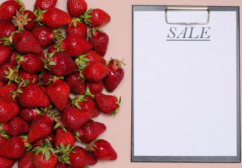 Juicy, ripe strawberries are laid out on a pink background with a tablet for recording for sale. Copy Space.