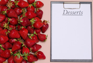 Juicy, ripe strawberries are laid out on a pink background with a tablet for recording dessert. Copy Space.