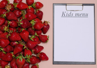 Juicy, ripe strawberries are laid out on a pink background with a tablet for recording the Copy Space children's menu.