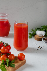 A glass of tomato juice, tomatoes in front. Behind is a jug of juice, pepper, salt and parsley.