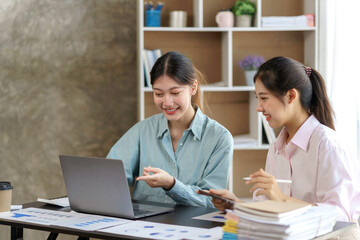 Two young beautiful Asian business woman in the conversation, exchanging ideas on laptop computer together at office.