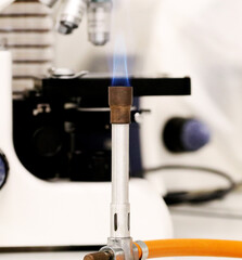 A bunsen burner, used in the microbiology laboratory, next to a microscope.