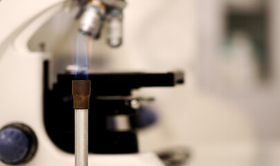 A bunsen burner, used in the microbiology laboratory, next to a microscope.