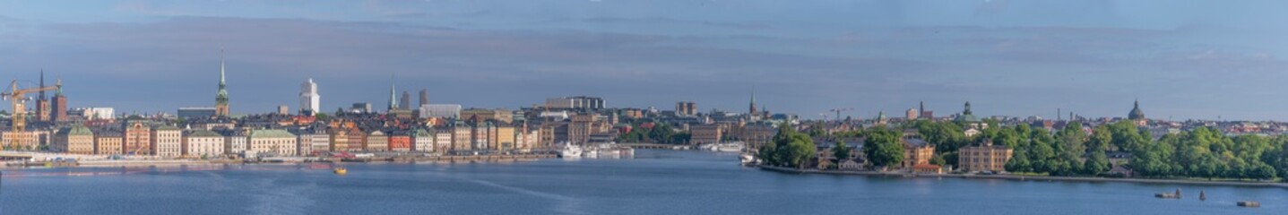 Panorama view at sunrise, the old town Gamla Stan, down town buildings, the islands Skeppsholmen and Kastellholmen at the bay Stockholms Ström with commuting boats a sunny summer day in Stockholm