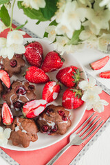 Fresh chocolate cakes with cranberry and strawberry on a white plate. Served table with fresh gluten free muffins, red napkin and jasmine flower.