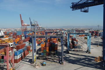 Container terminal with stowed containers from different shippers and gantry cranes in Valencia. In horizon is a city buildings and mountain under blue sky. - obrazy, fototapety, plakaty