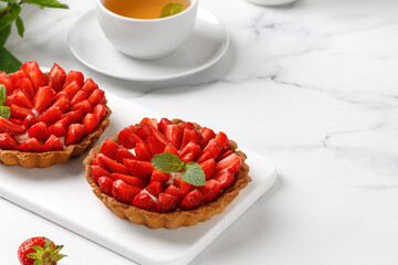 Homemade strawberry Tarts with cream decorated with mint leaves on white board and marble background. Tea time. Copy space.