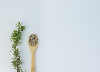 Wooden spoon with vitamins and rosemary branch on white background
