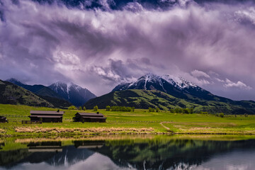 2022-06-10 ABSAROKA RANGE WITH SNOW AND A GREEN VALLEY WITH OUTBUILDINGS AND A REFLECTION IN A...
