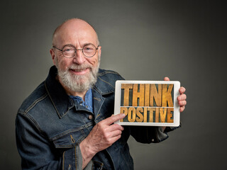 smiling senior man is showing a digital tablet with think positive sign in retro letterpress wood...