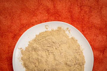maca root powder on white ceramic plate against red textured paper, superfood concept