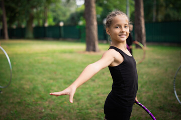 Girl doing exercise with hoop on rhythmic gymnastics training with other trainees outdoors in sports camp in summer