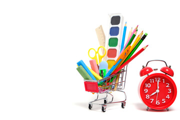 Shopping cart full school supplies and office supplies and red alarm clock white background.