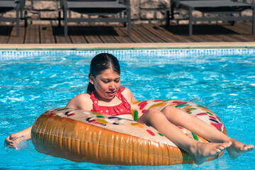 pretty young girl playing with her donut-shaped buoy in the swimming pool