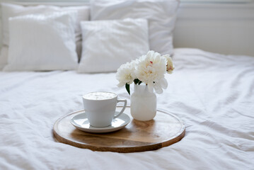 Fototapeta na wymiar Light cozy bedroom, Coffee or tea cup and an flowers on the white bed. Breakfast in bed. Coffee cup and flowers on a white bed. White Concept.