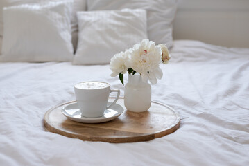 Fototapeta na wymiar Light cozy bedroom, Coffee or tea cup and an flowers on the white bed. Breakfast in bed. Coffee cup and flowers on a white bed. White Concept.