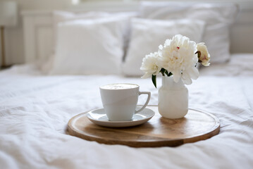 Obraz na płótnie Canvas Light cozy bedroom, Coffee or tea cup and an flowers on the white bed. Breakfast in bed. Coffee cup and flowers on a white bed. White Concept.