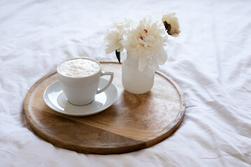 Light cozy bedroom, Coffee or tea cup and an flowers on the white bed. Breakfast in bed. Coffee cup and flowers on a white bed. White Concept.