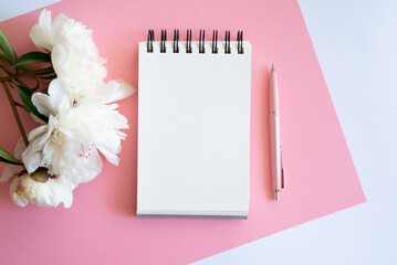 Top view of notebook with white empty page pink peonies and Feminine home office mock up with blank sheet of paper A4 portrait format, copy space for text. Flat lay. Pink peony and coffee