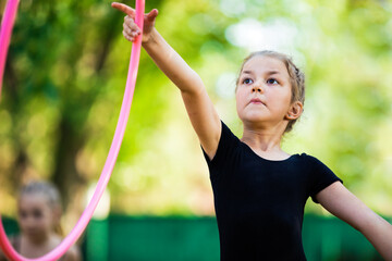 Girl doing exercise with hoop on rhythmic gymnastics training outdoors in summer in sports camp