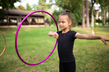 Girl doing exercise with hoop on rhythmic gymnastics training outdoors in summer in sports camp