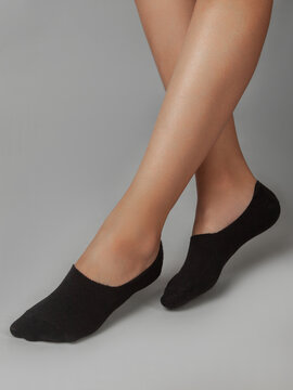 A cropped side view of a beautiful woman's legs in black socks, isolated against a gray background. Young woman walking on tiptoes. Comfortable footwear for ladies and girls. Cozy women's hosiery.