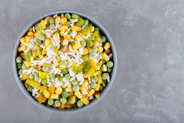 Bowl with mixed frozen vegetables with rice on a gray background. Frozen vegetables retaining all nutrients: green peas, corn, bell pepper. Healthy food concept. Top view. Copy space