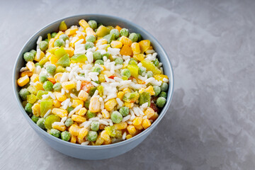 Bowl with mixed frozen vegetables with rice on a gray background. Frozen vegetables retaining all nutrients: green peas, corn, bell pepper. Healthy food concept. Top view. Copy space