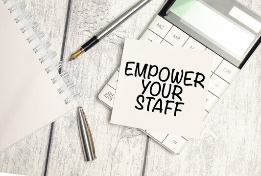 EMPOWER YOUR STAFF - text on white sticker and calculator with pen on wooden background